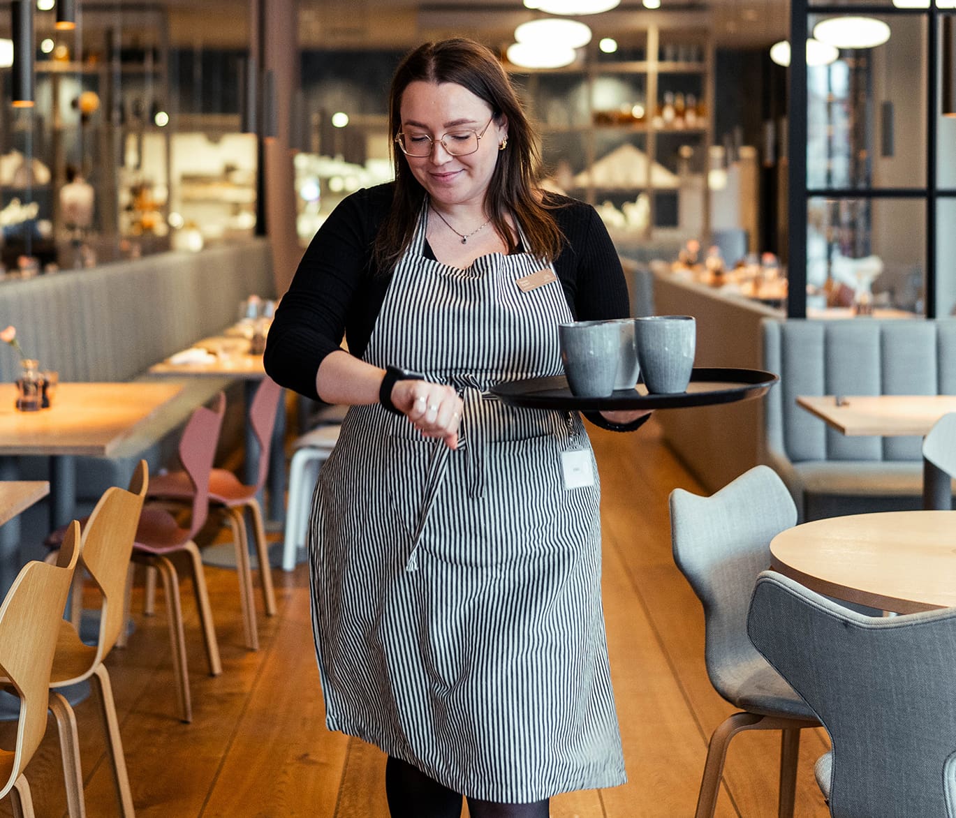 billede af en tjener kigger på sit solt pager ur med et fad med tre kopper kaffe